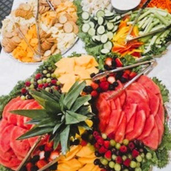 A vibrant buffet spread featuring fruit, vegetable, and cracker platters, with serving tongs.