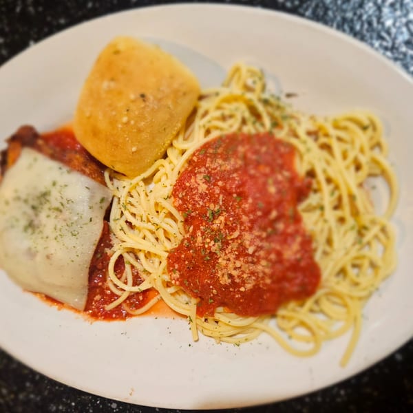Chicken parmesan with spaghetti, marinara sauce, and a bread roll on a white plate.