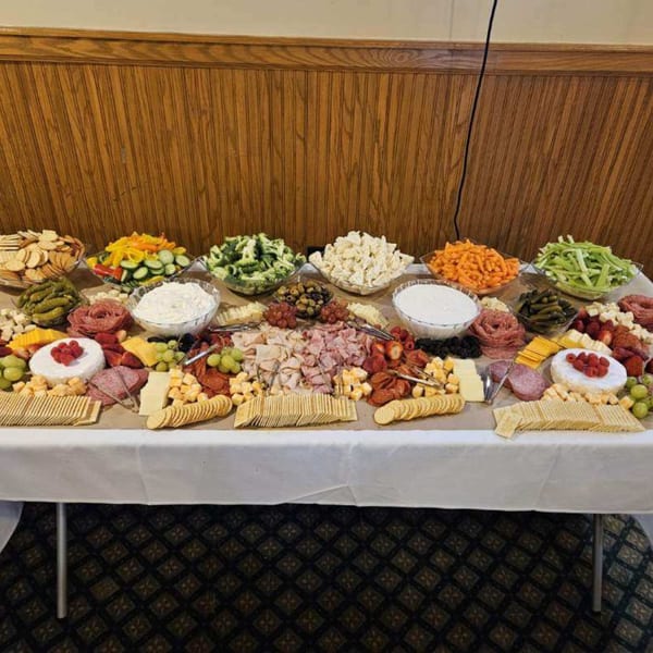 A long buffet table laden with a variety of Italian appetizers, including meats, cheeses, crackers, and vegetables.
