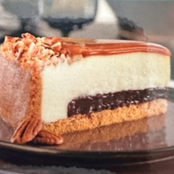 A slice of layered cake with white, chocolate, and orange layers, topped with caramel and pecans.