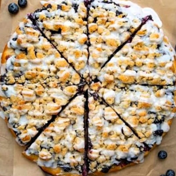 Blueberry dessert pizza with white icing and crumble topping, sliced into eight pieces.