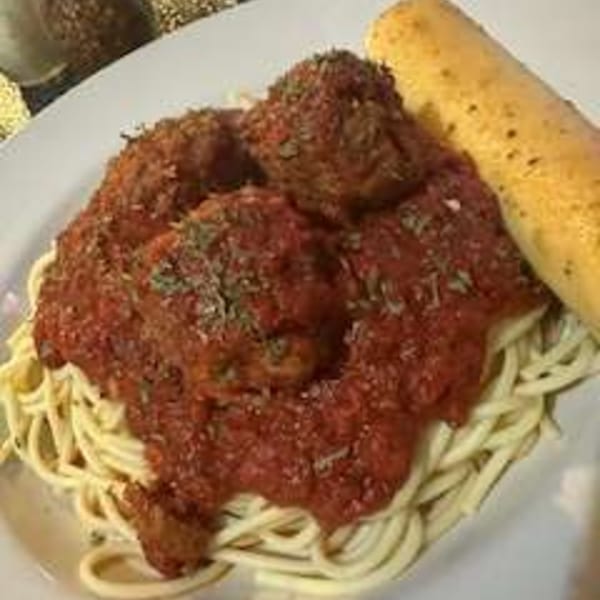 Spaghetti with meatballs and red sauce, garnished with herbs, served with a breadstick.