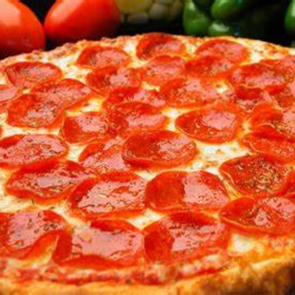 Close-up of a pepperoni pizza with melted cheese, with tomatoes and green peppers in the background.