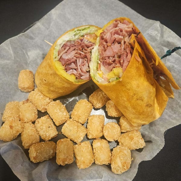 A large wrap filled with meat and lettuce, cut in half, served with tater tots.