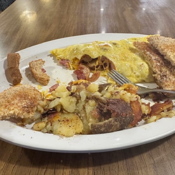 A breakfast plate with a cheese and bacon omelet, home fries, and toast on a wooden table.