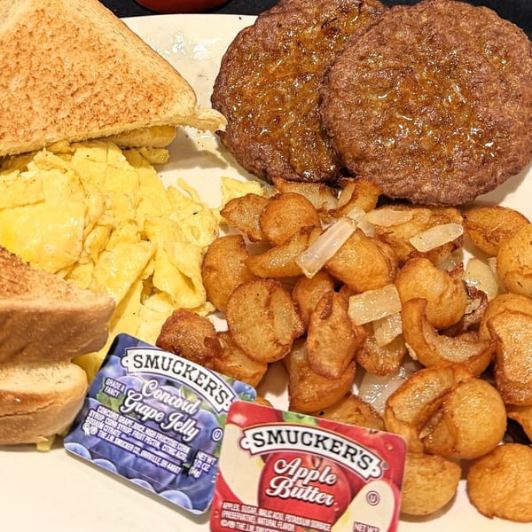 A breakfast plate with scrambled eggs, sausage patties, home fries, toast, grape jelly, and apple butter.