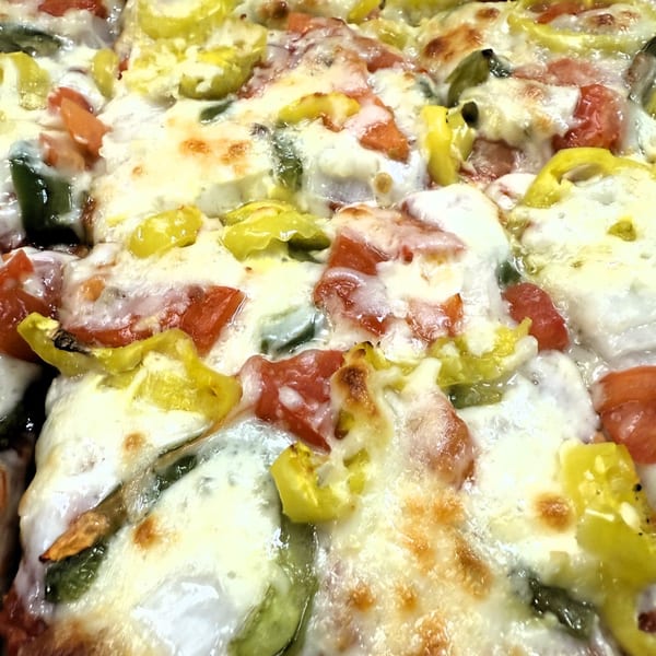 Close-up of a Tony M's pizza with melted cheese, red tomatoes, and yellow banana peppers.