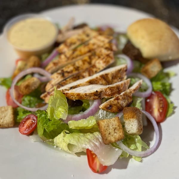 Grilled chicken salad with lettuce, tomatoes, red onions, croutons, and a side of dressing.