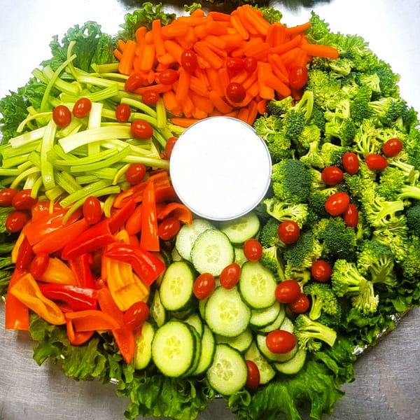 A vibrant vegetable platter with carrots, celery, broccoli, bell peppers, cucumbers, cherry tomatoes, and dip.