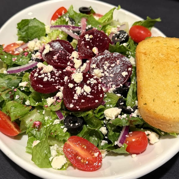 A vibrant Italian salad with beets, feta, olives, tomatoes, and red onion, served with garlic bread.