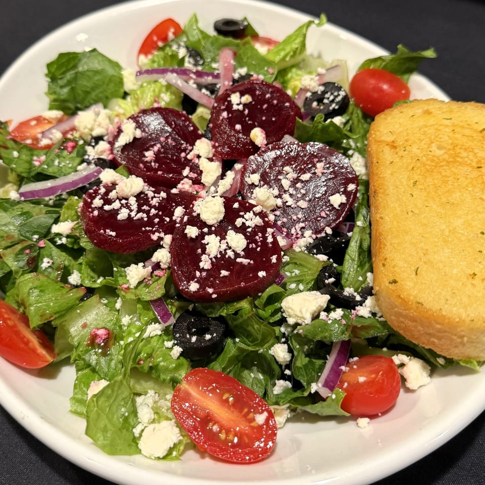 A vibrant Italian salad with beets, feta, olives, tomatoes, and red onion, served with garlic bread.