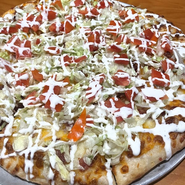 Tony M's taco pizza, topped with shredded lettuce, diced tomatoes, and a creamy white sauce.