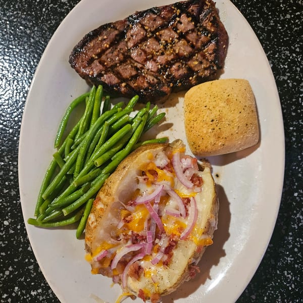 Grilled steak with green beans, a loaded baked potato, and a dinner roll on a white plate.