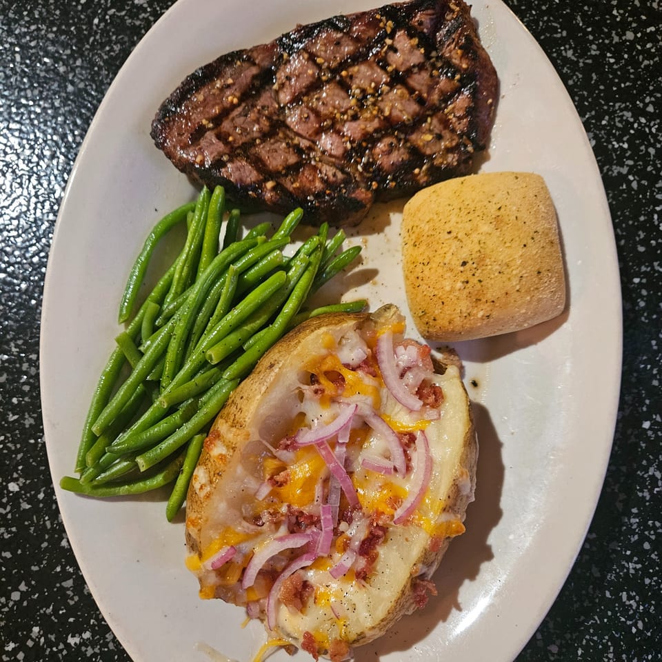 Grilled steak with green beans, a loaded baked potato, and a dinner roll on a white plate.