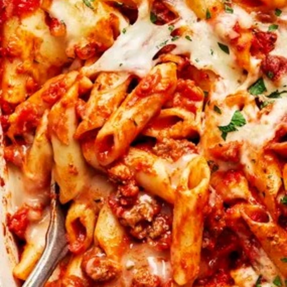 Close-up of baked ziti with melted cheese, rich red sauce, and ground meat, garnished with parsley.