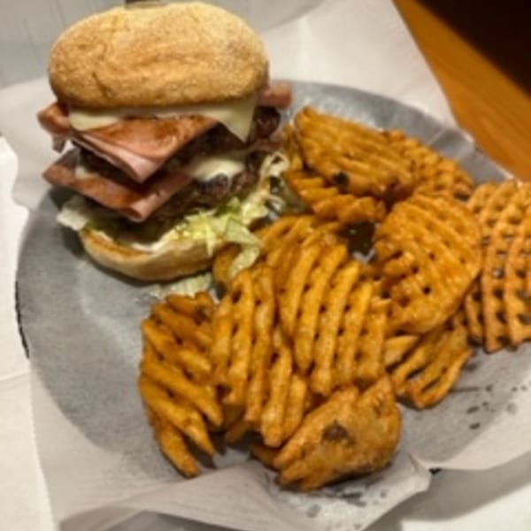 A large burger with multiple patties and ham, served with a side of waffle fries.