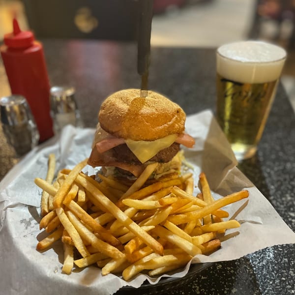 A large burger with cheese and bacon, served with a side of fries and a glass of beer.