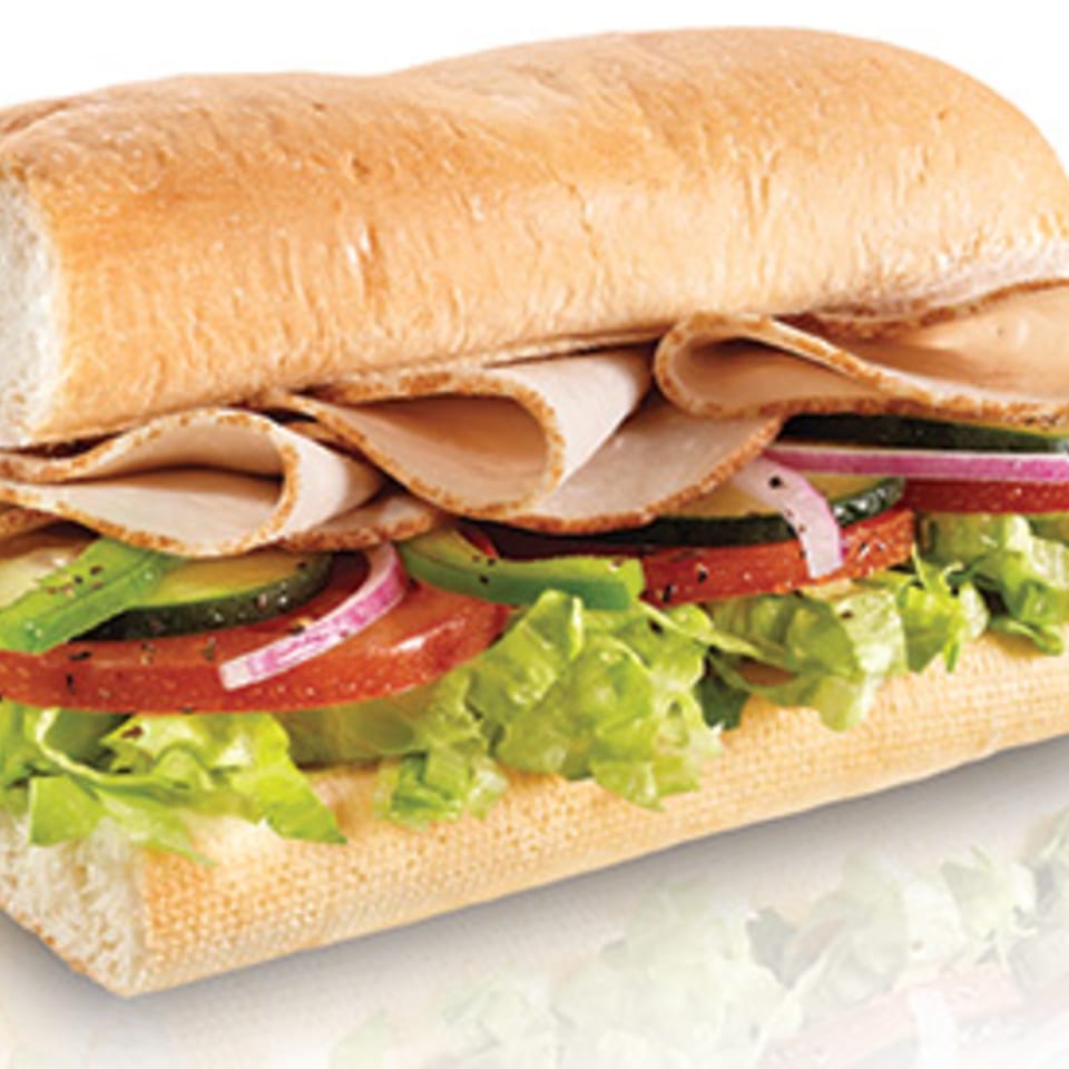 A large Italian sub sandwich with turkey, lettuce, tomatoes, onions, and cucumbers.
