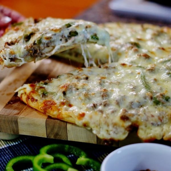 A slice of cheesy Italian pizza with sausage and green peppers being lifted from the pie.