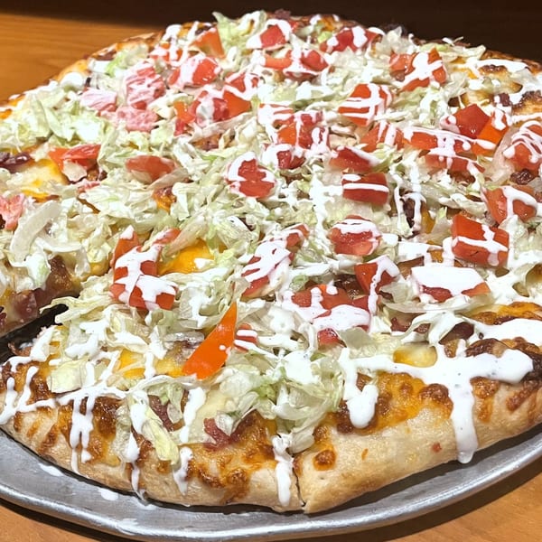 A Tony M's Italian pizza topped with shredded lettuce, diced tomatoes, and a creamy white sauce.