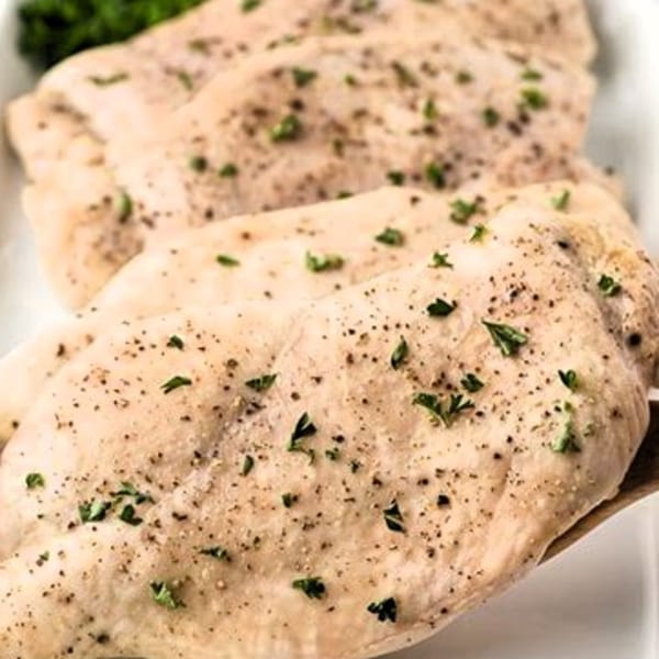 Three seasoned chicken breasts with parsley and black pepper on a white platter.