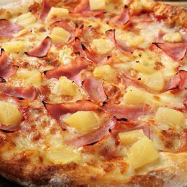 Close-up of a Hawaiian pizza with melted cheese, ham, and pineapple chunks.