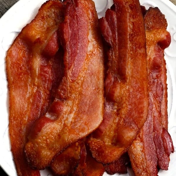 Crispy strips of bacon, golden brown and reddish, piled on a white plate.