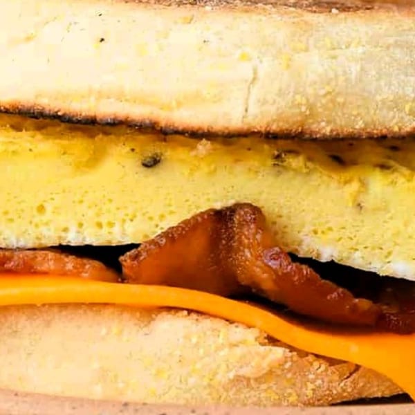 Close-up of a breakfast sandwich with egg, bacon, and cheese on toasted bread.