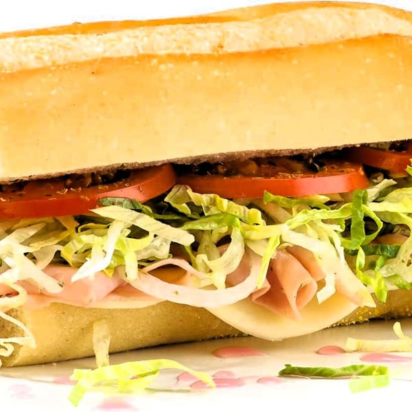 A close-up of a large Italian sub sandwich filled with ham, cheese, lettuce, tomatoes, and onions.