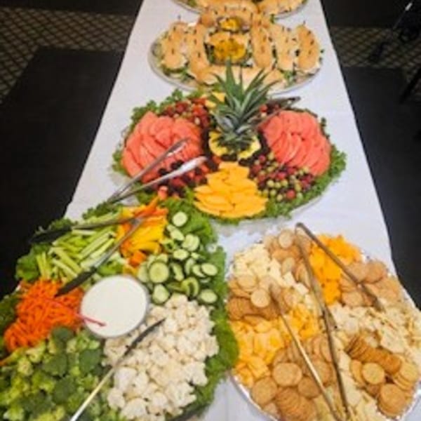 A buffet spread with fruit, cheese, crackers, and vegetables on a white tablecloth.