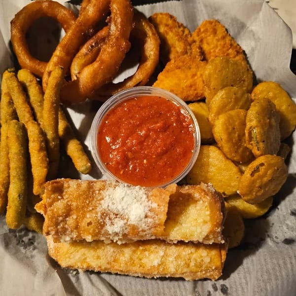 A basket of fried appetizers including onion rings, mozzarella sticks, fried pickles, and green beans with marinara.