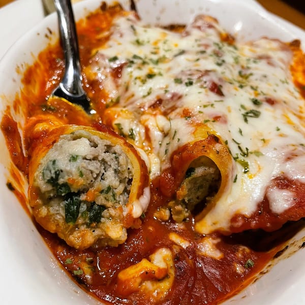 Baked manicotti with meat and spinach filling, topped with melted mozzarella and marinara sauce.