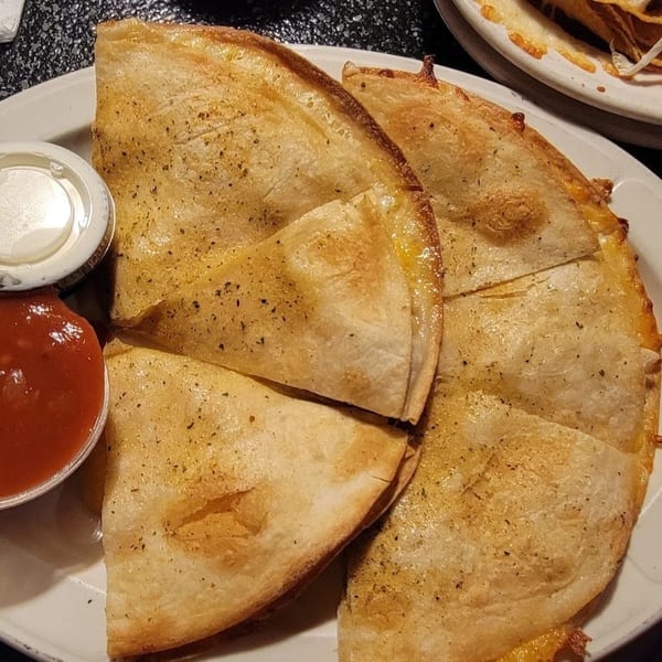 Golden-brown quesadilla wedges, seasoned with herbs, served with a side of red salsa and sour cream.