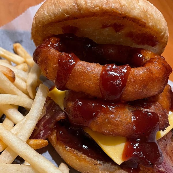 Close-up of a burger with cheese, bacon, onion rings, BBQ sauce, and a side of fries.