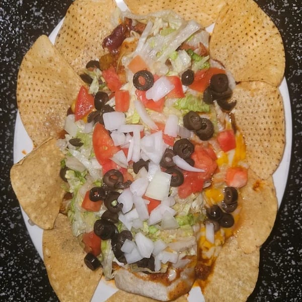 A plate of nachos with lettuce, tomatoes, black olives, and onions, surrounded by tortilla chips.