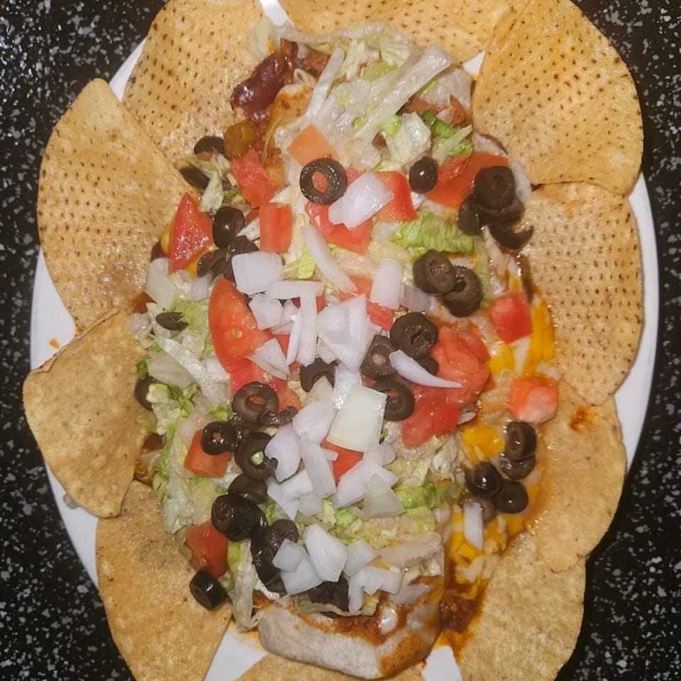 A plate of nachos with lettuce, tomatoes, black olives, and onions, surrounded by tortilla chips.