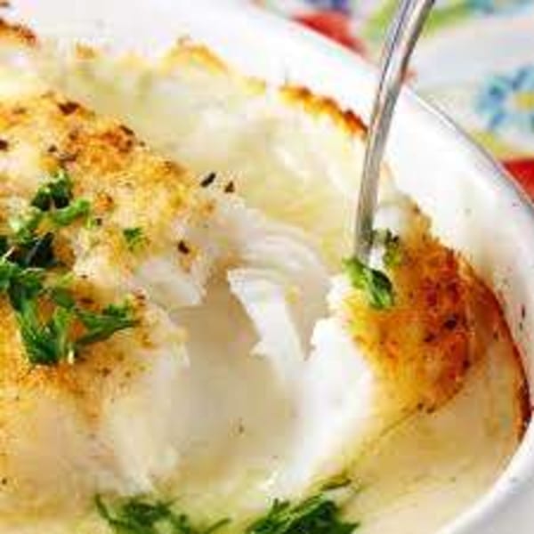 Baked white fish with a golden crust and green herbs, served in a white dish with a fork.