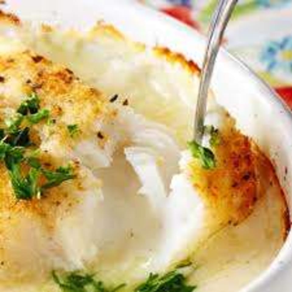 Baked white fish with a golden crust and green herbs, served in a white dish with a fork.