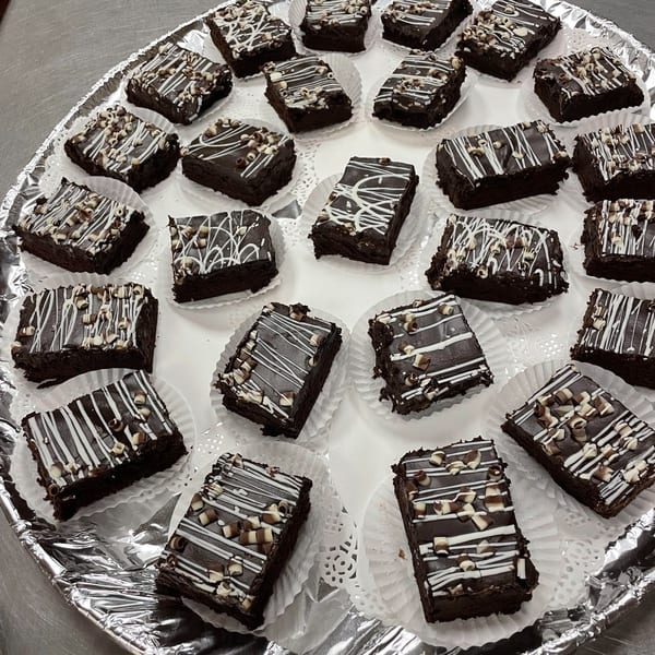 A tray of Tony M's chocolate brownies with white icing and chocolate shavings.