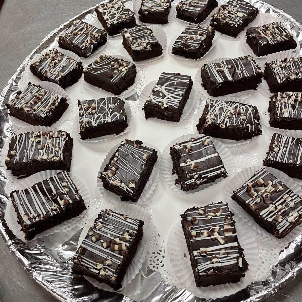 A tray of Tony M's chocolate brownies with white icing and chocolate shavings.