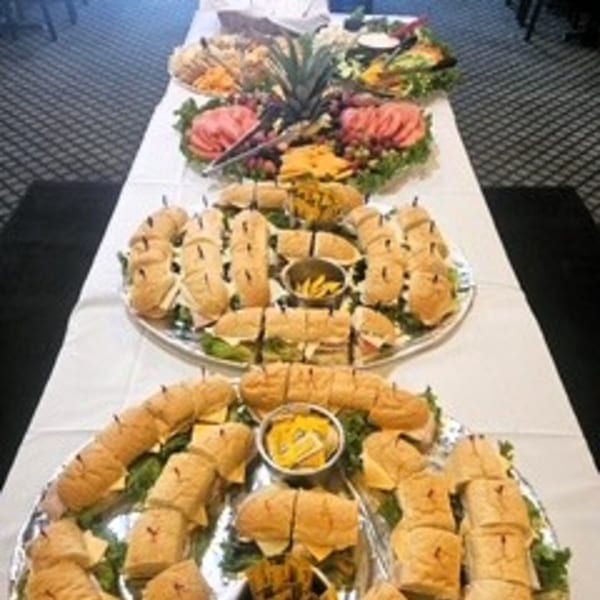 A long table laden with platters of Italian deli sandwiches, meats, cheeses, and fruit.
