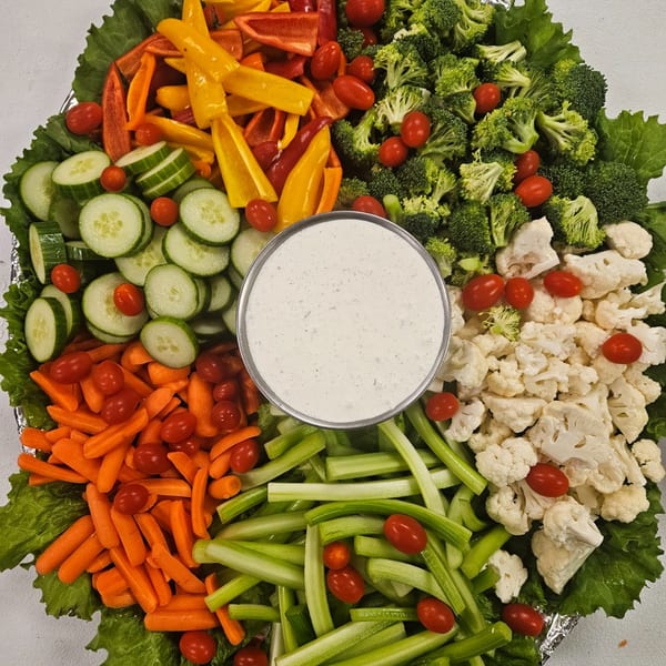 A colorful vegetable platter with broccoli, cauliflower, carrots, celery, bell peppers, cucumbers, cherry tomatoes, and a central dip.