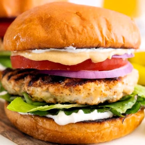 Grilled chicken sandwich with lettuce, tomato, red onion, and sauces on a brioche bun.