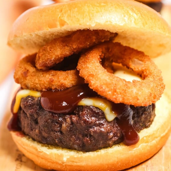 A juicy burger with melted cheese, barbecue sauce, and crispy onion rings on a bun.