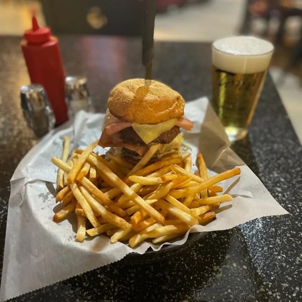 A large burger with cheese and bacon, a side of fries, and a glass of beer.