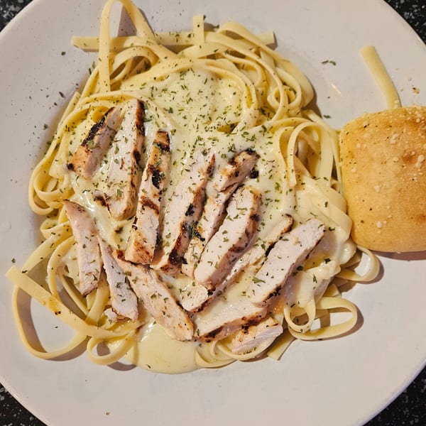 Tony M's grilled chicken fettuccine alfredo with parsley and a side of garlic bread.
