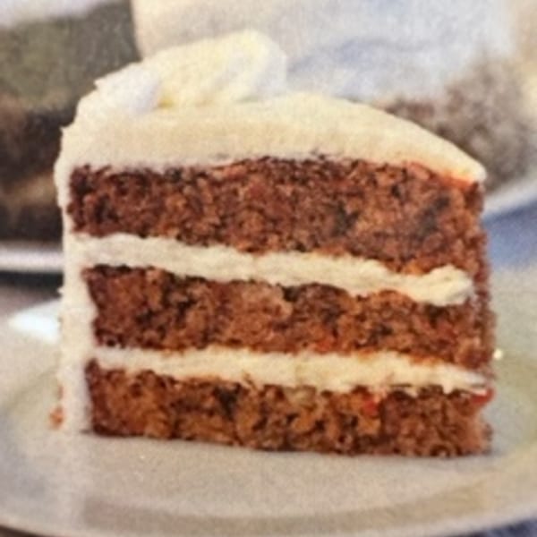 A slice of carrot cake with three layers of cake and white cream cheese frosting.