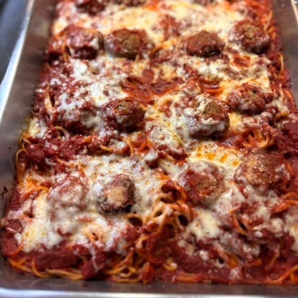Baked spaghetti with meatballs, marinara sauce, and melted cheese in a metal pan.