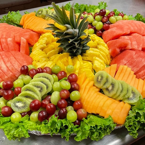 A vibrant fruit platter with watermelon, pineapple, kiwi, cantaloupe, and grapes on a bed of lettuce.